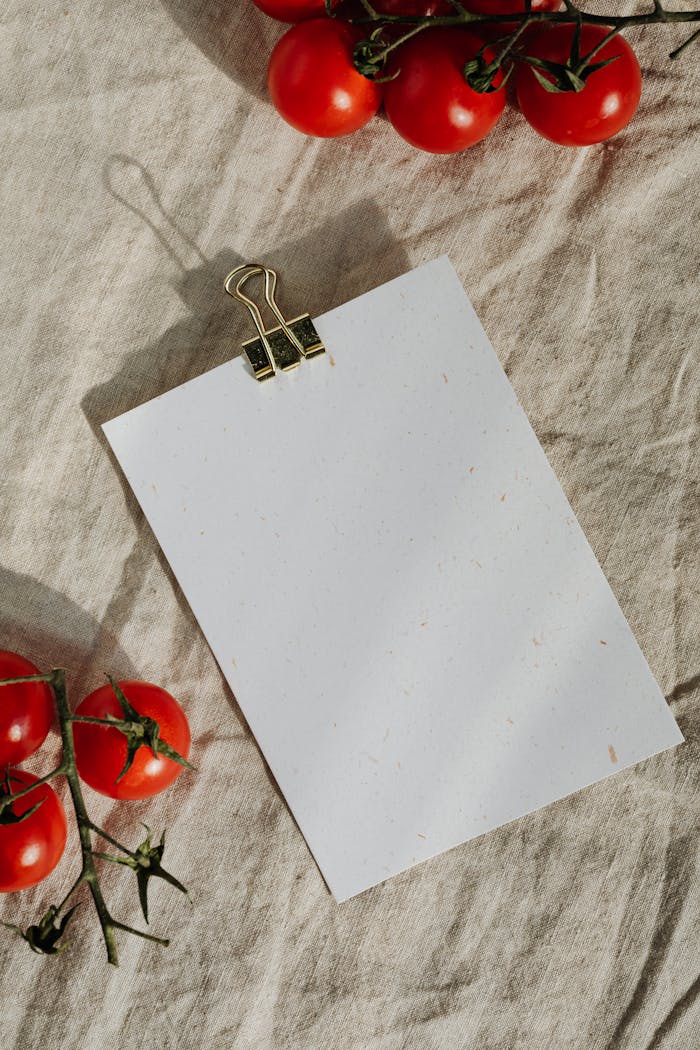 Blank sheet of paper with tomatoes on linen cloth, perfect for a food-themed flat lay.
