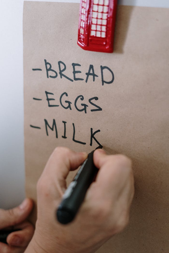 Close-up of a hand writing a grocery list with a marker on brown paper.