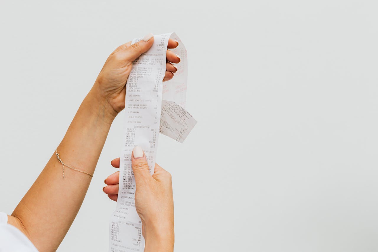 A detailed view of a person holding a long shopping receipt against a plain background.